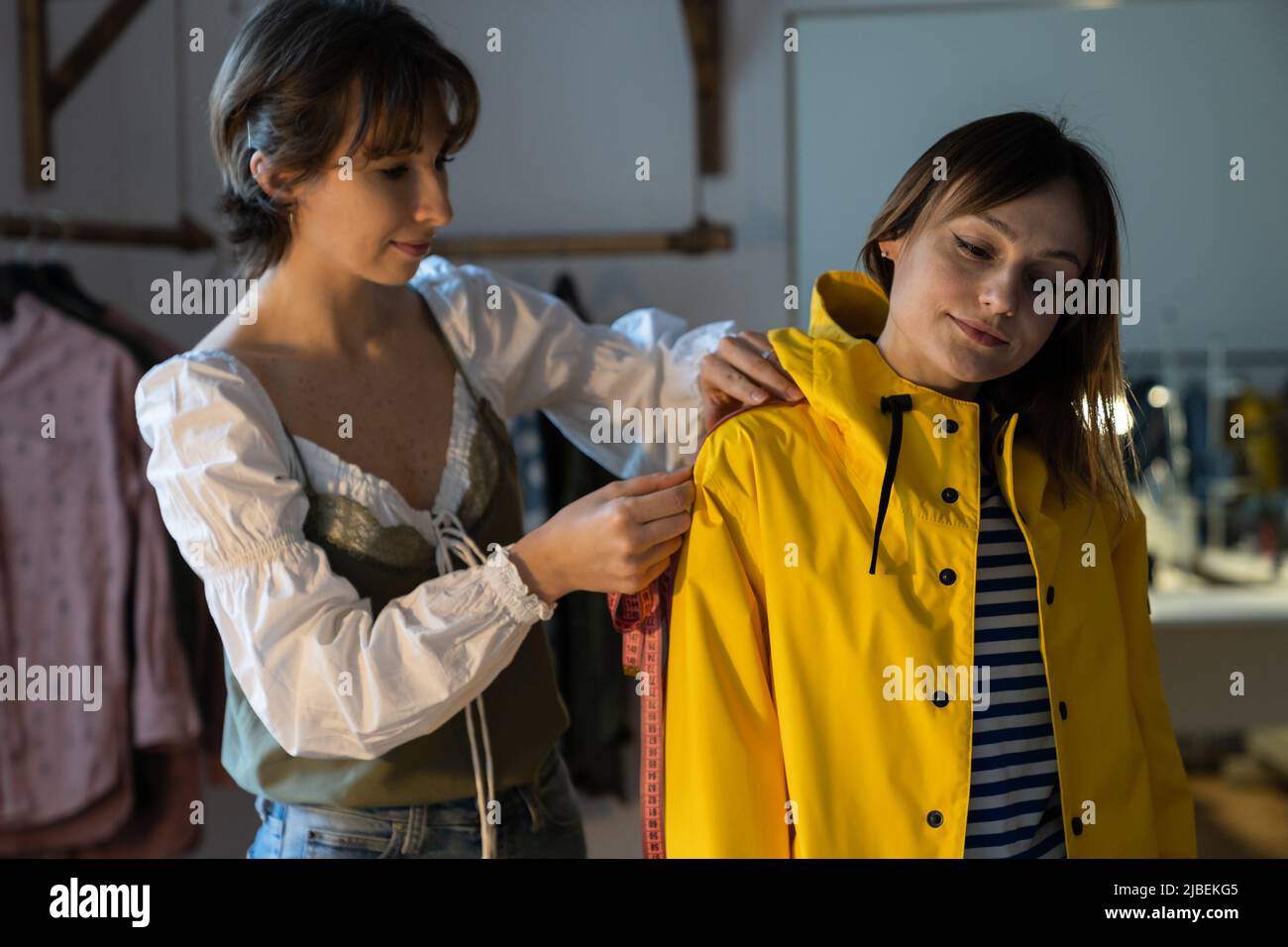 Fashion designer with female tailor measuring and fitting bespoke yellow rain jacket