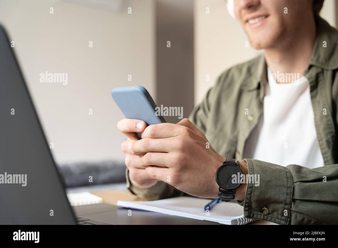 Closeup of male hand holds mobile phone while working on laptop selective focus Stock Photo