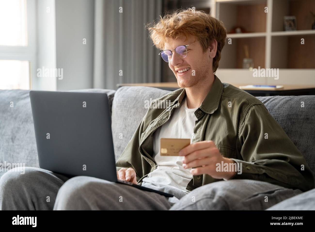 Successful freelancer ginger man holding credit card, using laptop Stock Photo