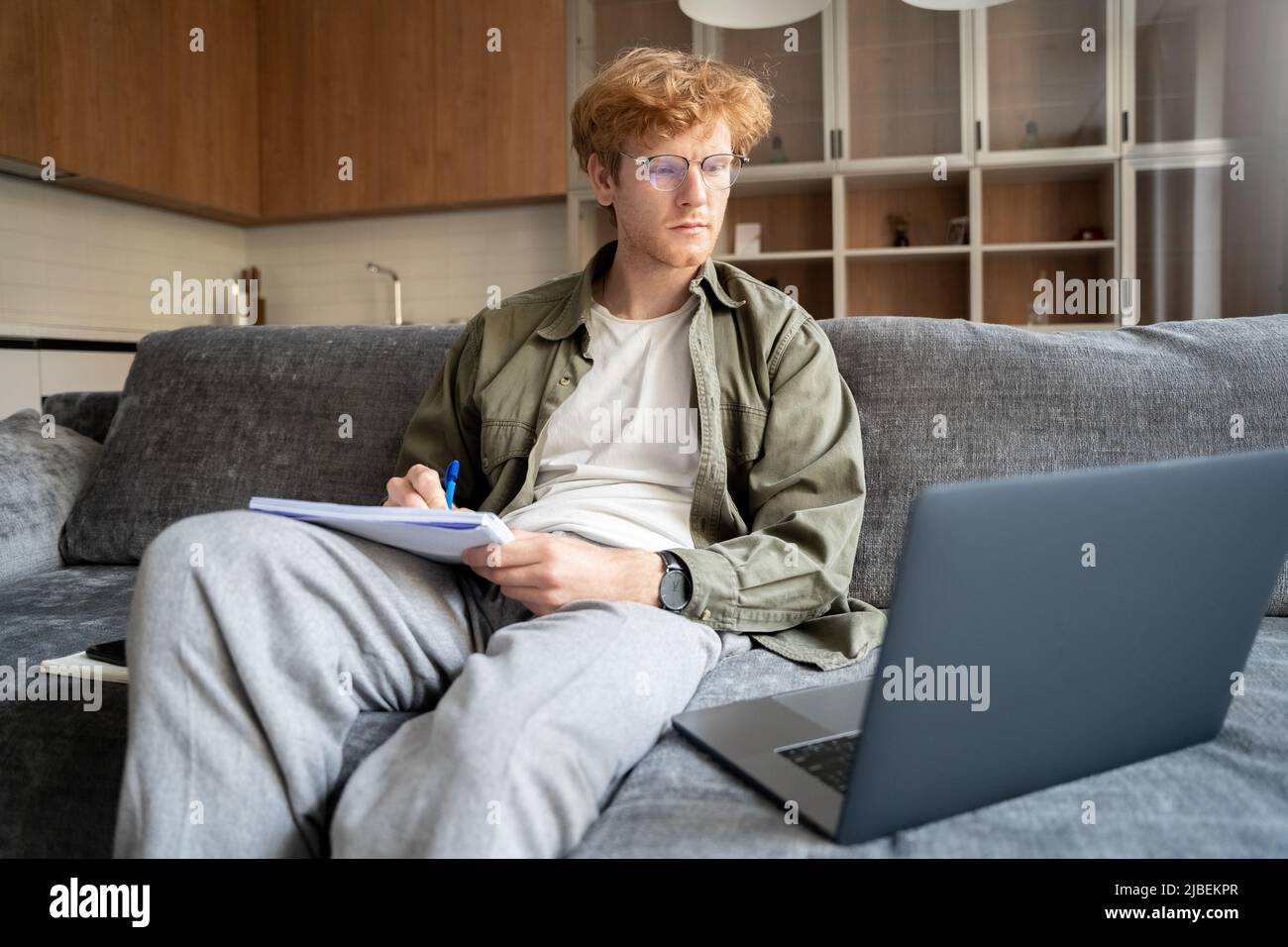 Focused young ginger irish man watching webinar video course writing notes Stock Photo