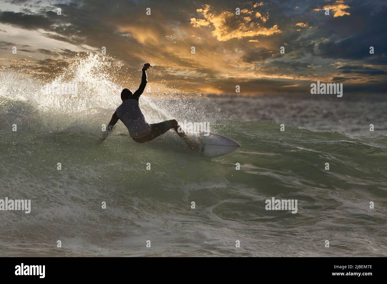 Dramtic silhouetted surfer on a high energy wave at sunset. Stock Photo