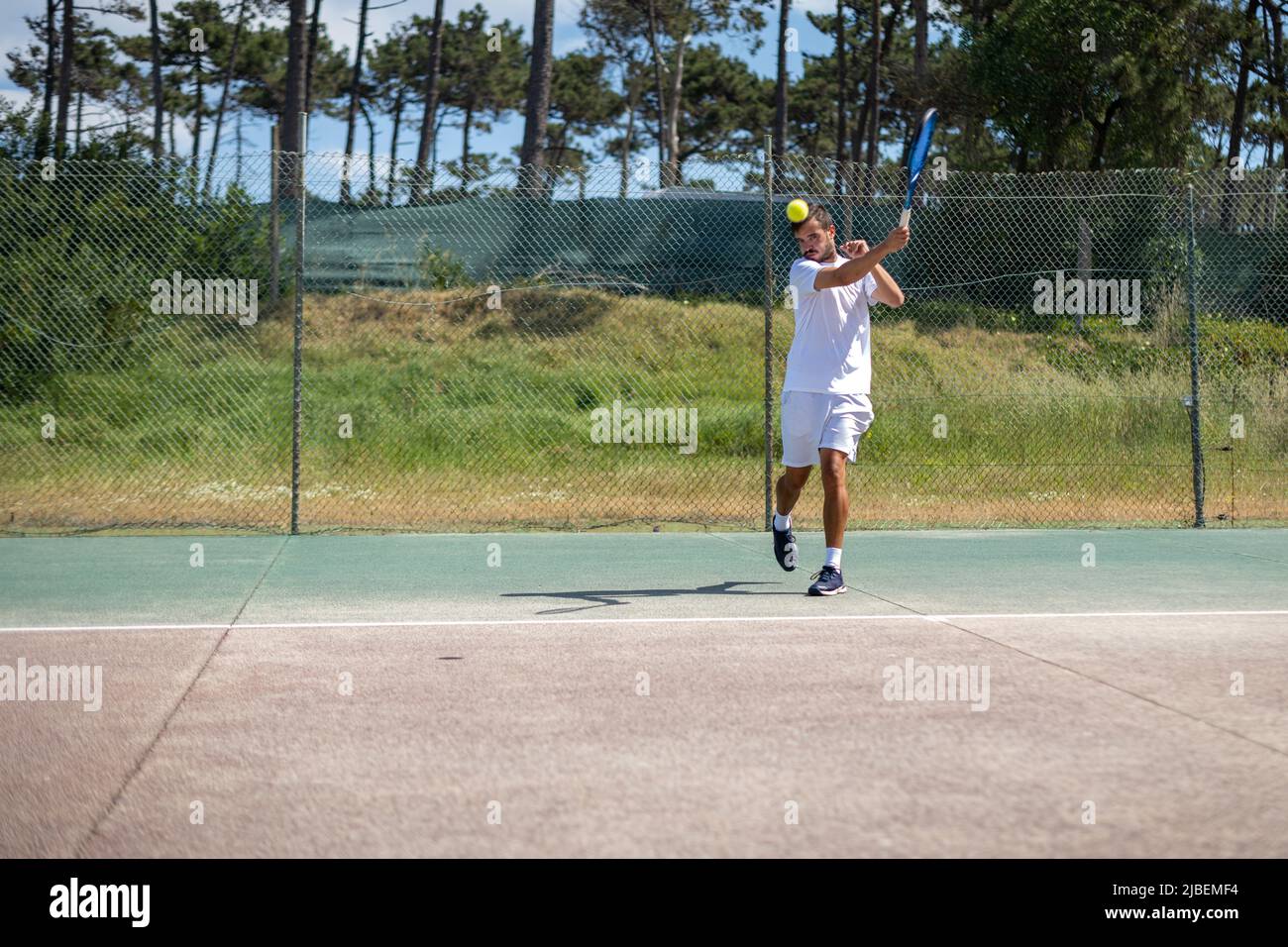Tennis player hitting forehand at ball with racket on court Stock Photo