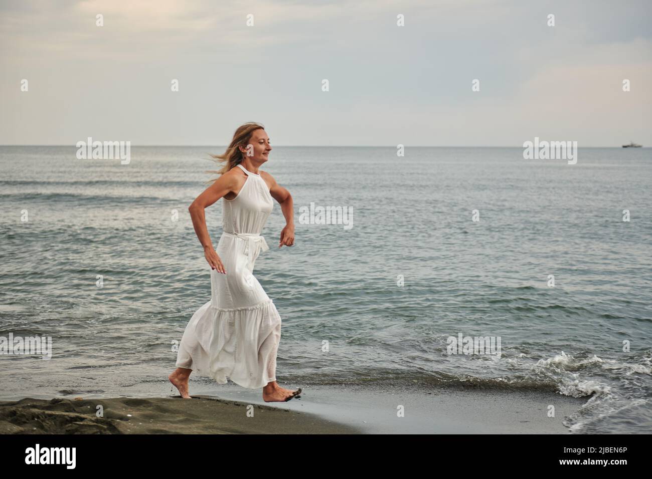 a girl in a white dress runs along the shore Stock Photo - Alamy