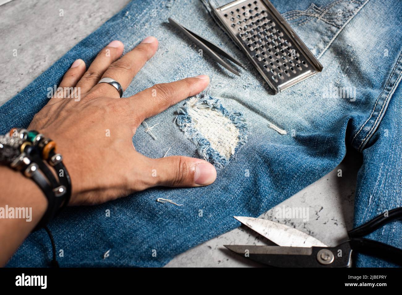 The man making ditressed jeans. DIY ripped jeans with scissors and razor  Stock Photo - Alamy