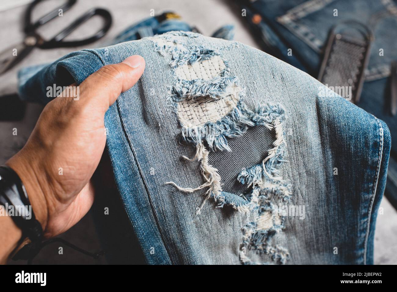The man making ditressed jeans. DIY ripped jeans with scissors and razor  Stock Photo - Alamy