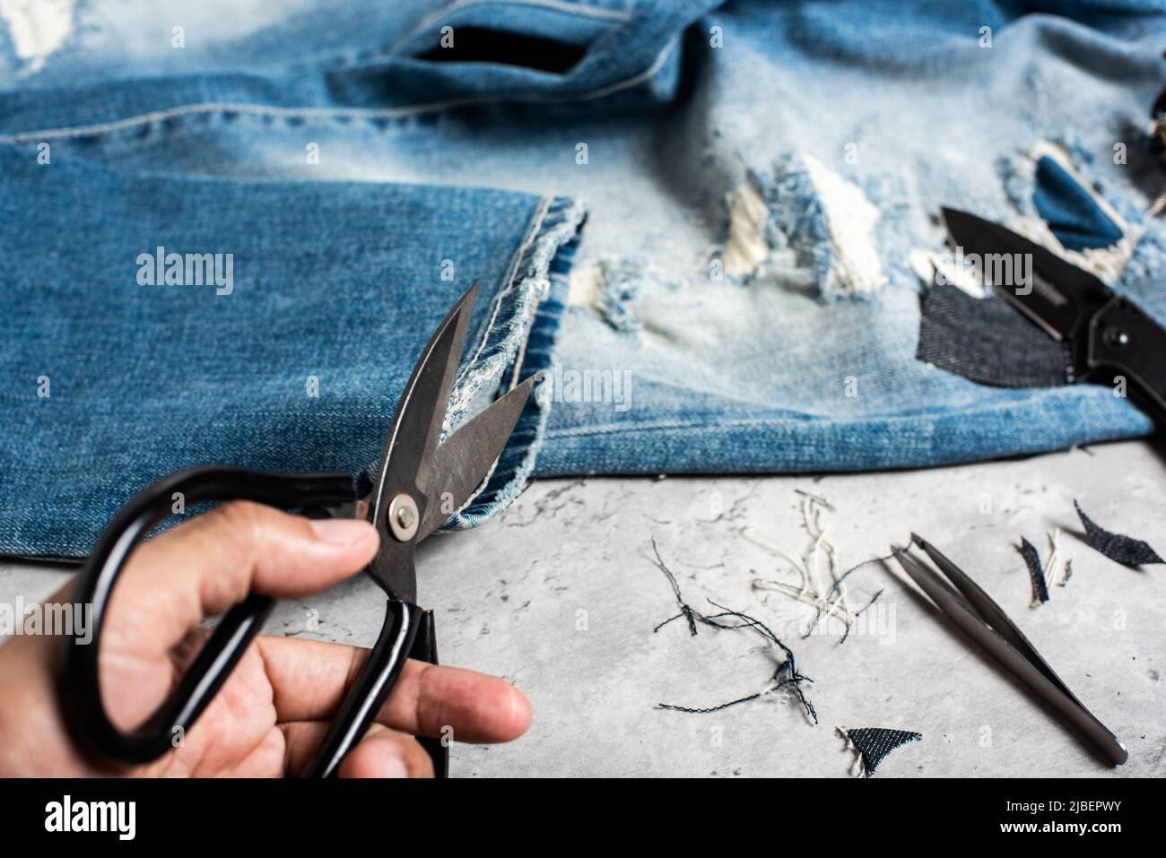 The man making ditressed jeans. DIY ripped jeans with scissors and