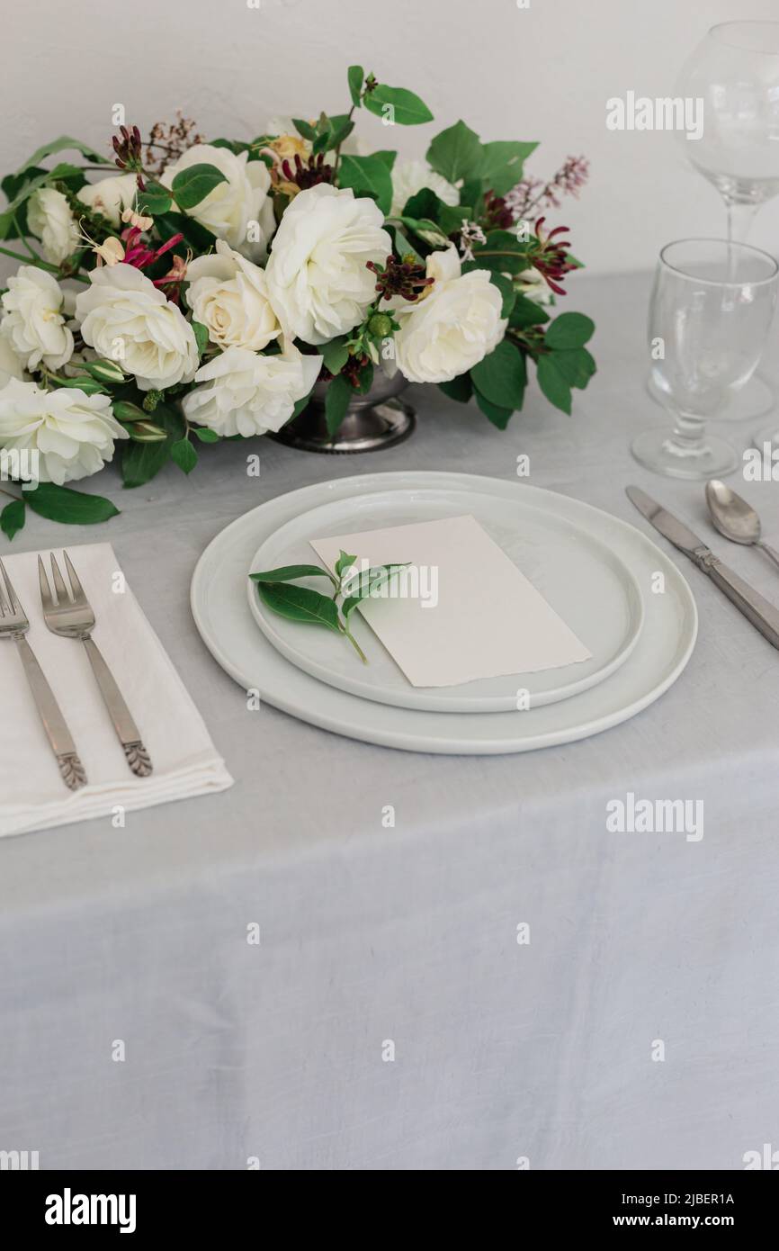 A beautiful white rose floral arrangement on a dinner table with candles on iit. Gray and white palette. Wedding design website or workshop. Stock Photo