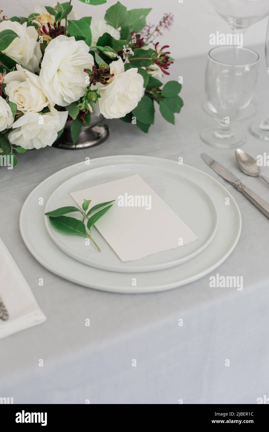 A beautiful white rose floral arrangement on a dinner table with candles on iit. Gray and white palette. Wedding design website or workshop. Stock Photo