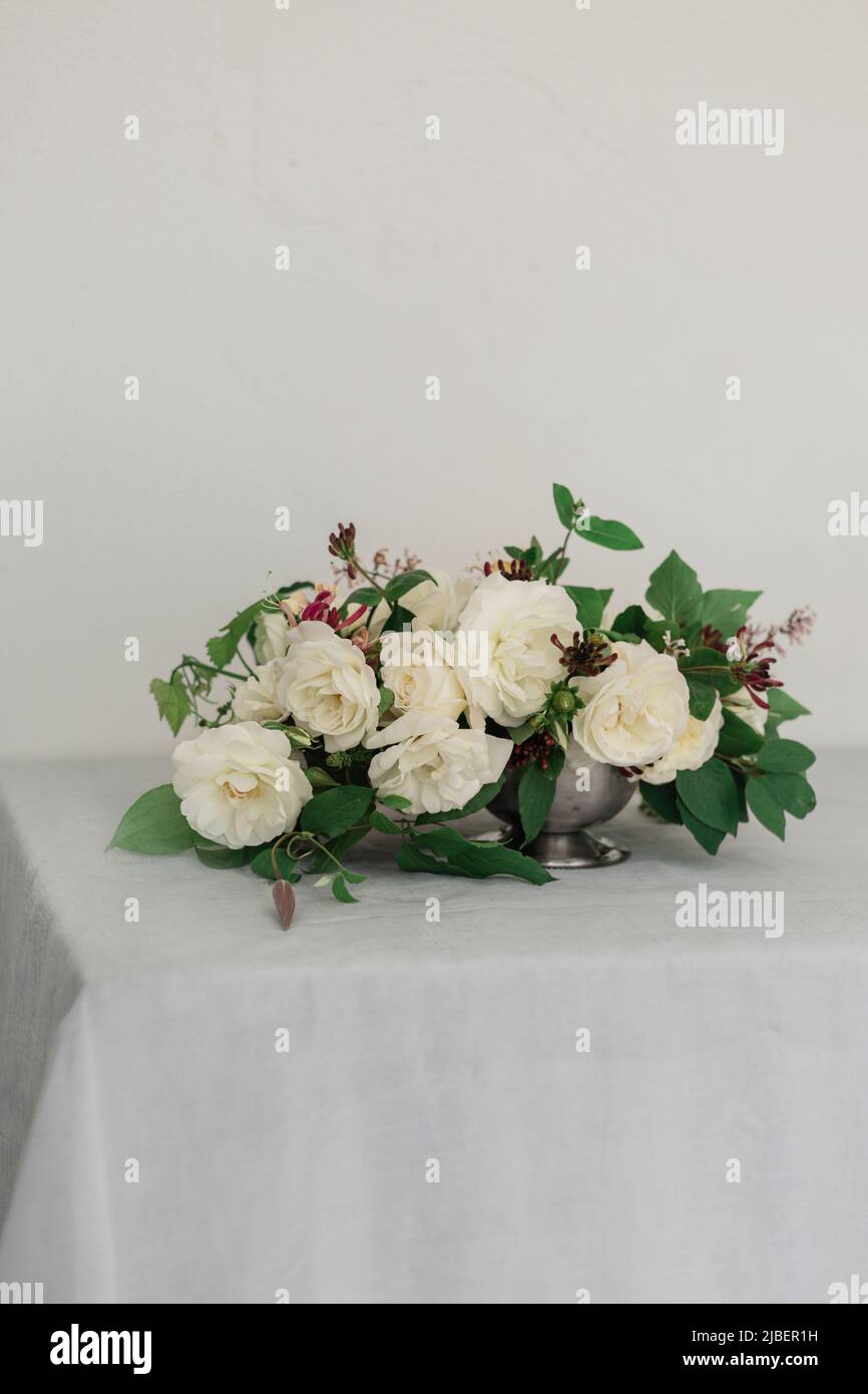 A beautiful white rose floral arrangement on a dinner table with candles on iit. Gray and white palette. Wedding design website or workshop. Stock Photo