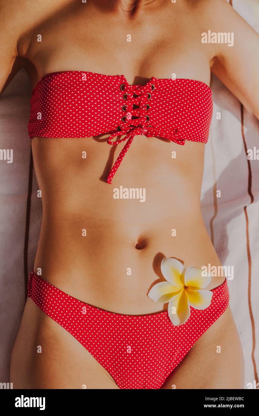 Bikini body woman sunbathing tanning in summer sun for tanned skin vertical closeup. Red swimsuit and feminine flower on the hips for spa beauty Stock Photo