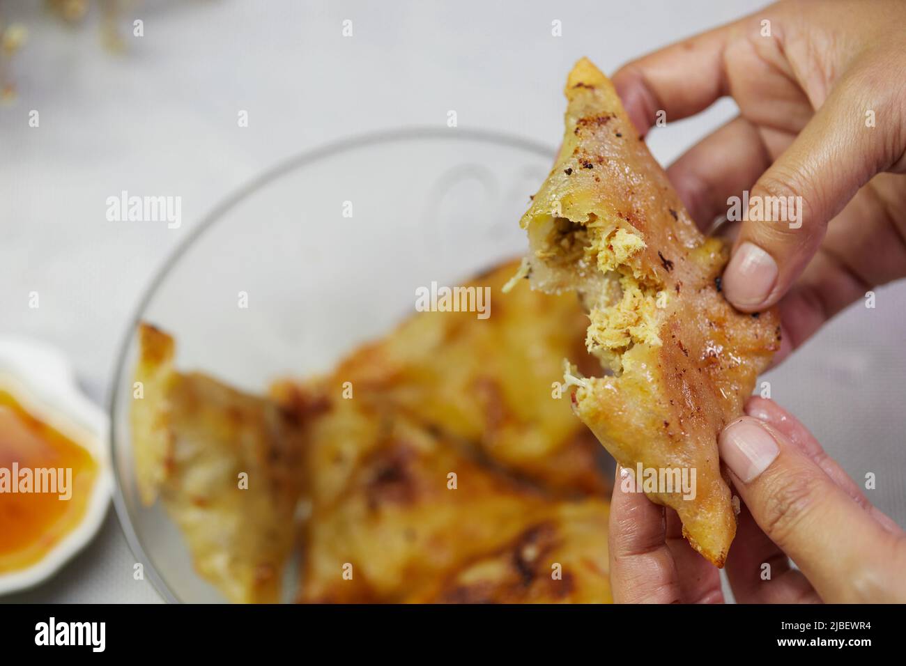Woman hand holding Samosa with sauce on white tablecloth Stock Photo