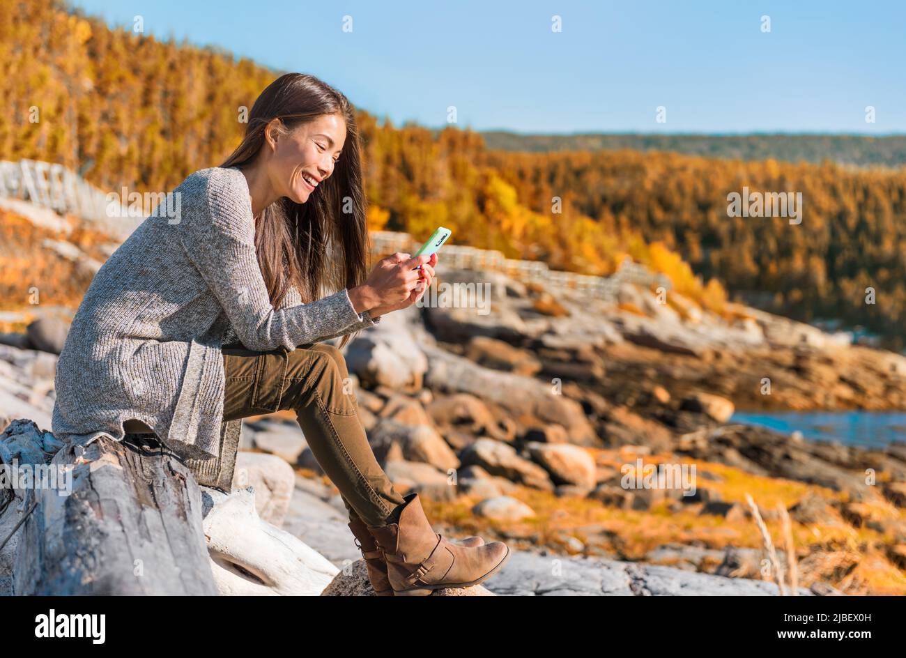 Mobile phone travel lifestyle Asian woman using cellphone data durig outdoor hiking adventure in Quebec, Canada. Happy girl texting in forest autumn Stock Photo