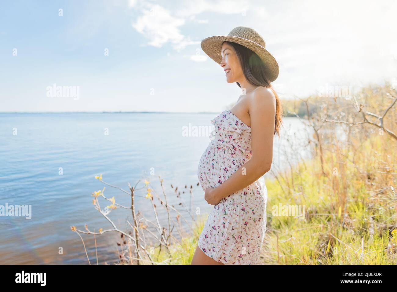 Pregnant Asian woman wearing sun hat during spring nature walk by the
