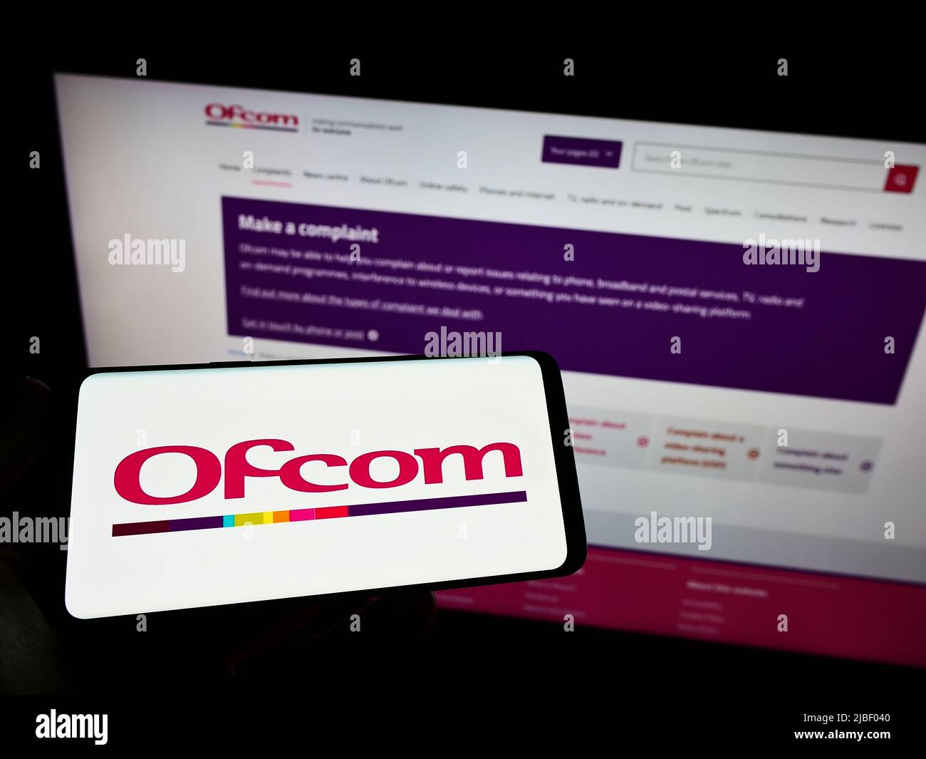 Person holding smartphone with logo of UK authority Office of Communications (Ofcom) on screen in front of website. Focus on phone display. Stock Photo
