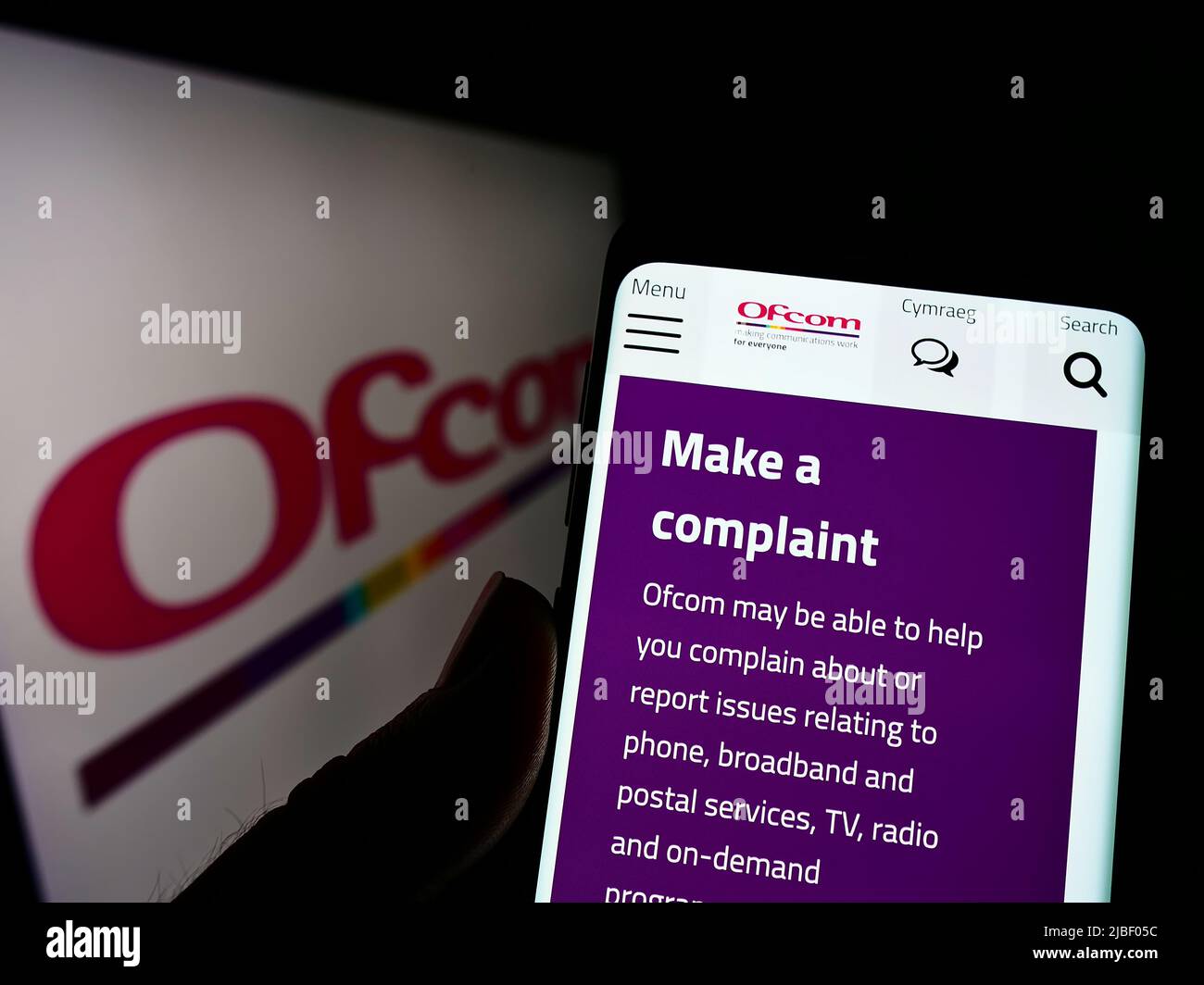 Person holding cellphone with website of UK authority Office of Communications (Ofcom) on screen with logo. Focus on center of phone display. Stock Photo