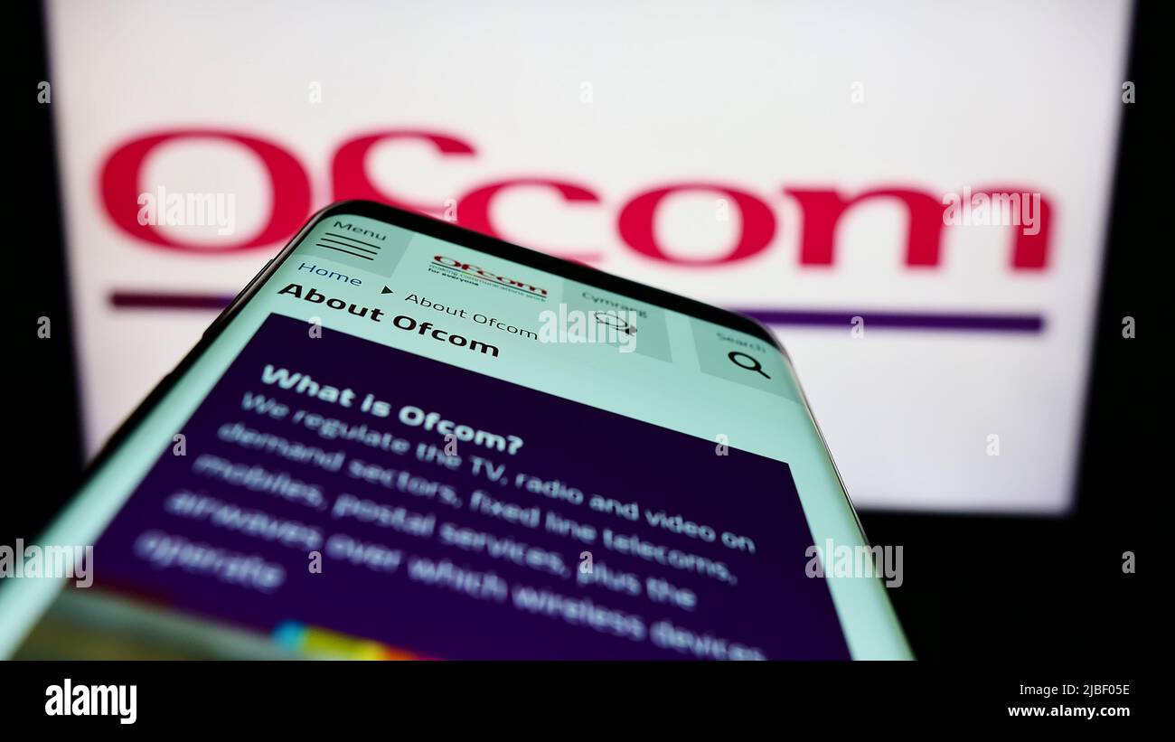 Mobile phone with webpage of UK authority Office of Communications (Ofcom) on screen in front of logo. Focus on top-left of phone display. Stock Photo