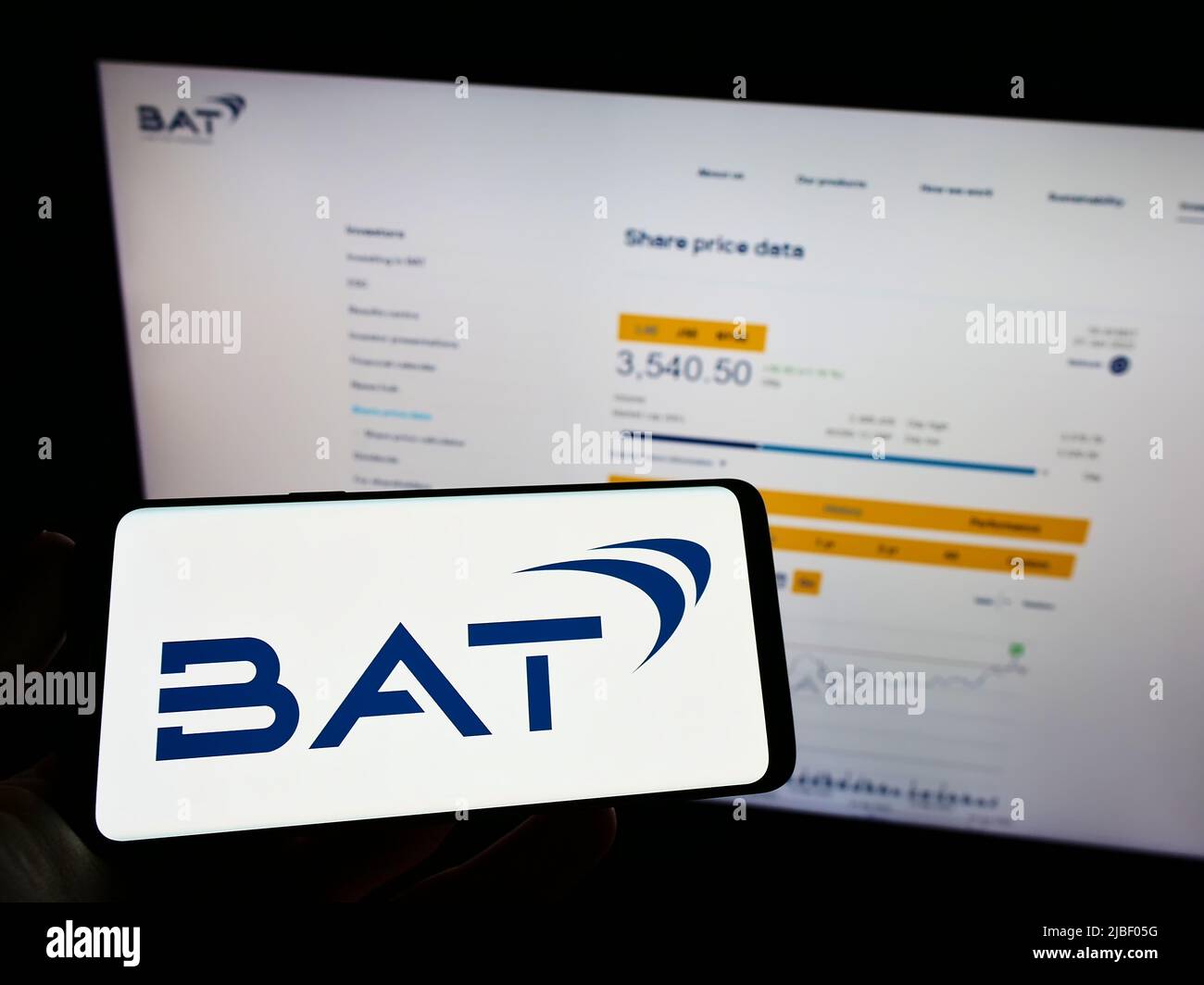 Person holding mobile phone with logo of company British American Tobacco plc (BAT) on screen in front of webpage. Focus on phone display. Stock Photo