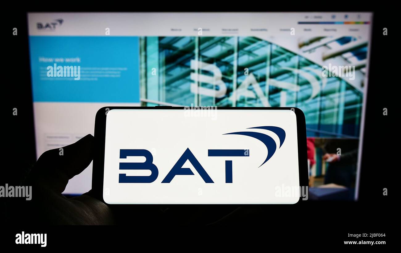 Person holding cellphone with logo of company British American Tobacco plc (BAT) on screen in front of business webpage. Focus on phone display. Stock Photo