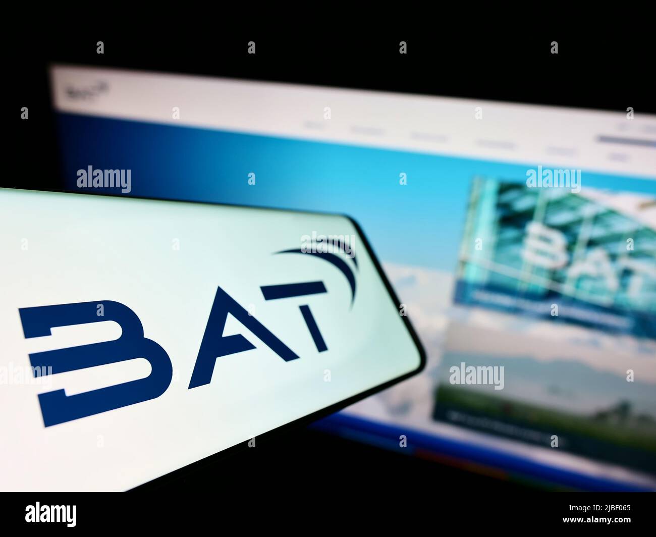 Mobile phone with logo of company British American Tobacco plc (BAT) on screen in front of website. Focus on center-left of phone display. Stock Photo