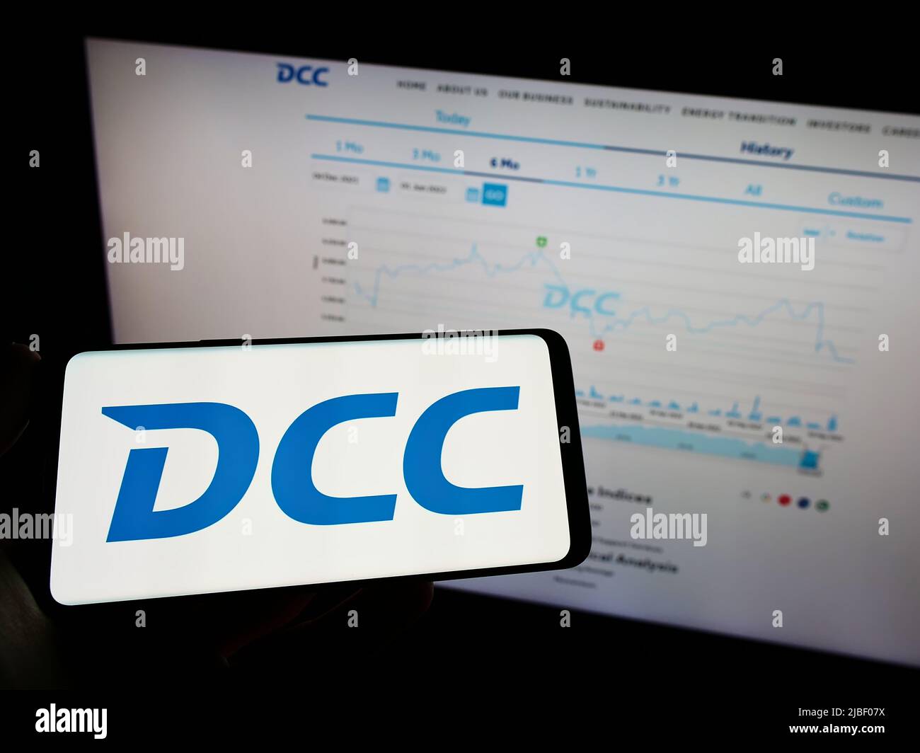 Person holding mobile phone with logo of Irish sales and marketing company DCC plc on screen in front of business web page. Focus on phone display. Stock Photo