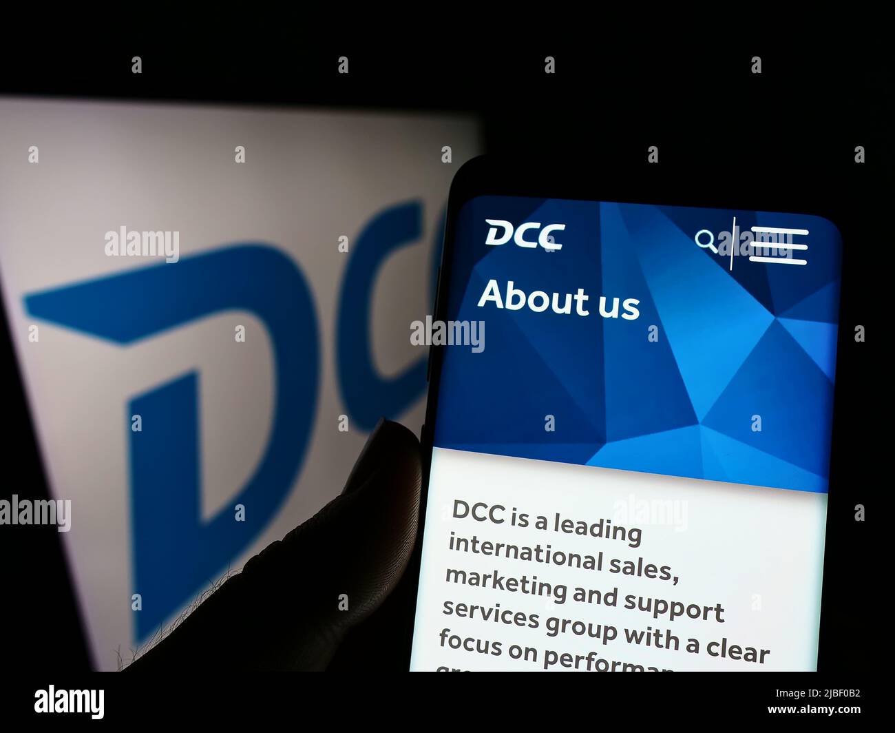 Person holding cellphone with webpage of Irish sales and marketing company DCC plc on screen in front of logo. Focus on center of phone display. Stock Photo