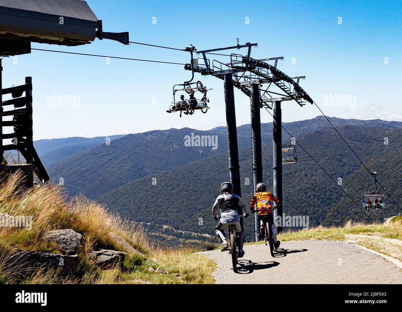 Two mountain bikers head off down the mountainfrom Eagles Nest as another group arrives on the Kosciuszko Express Chairlift from Thredbo Stock Photo