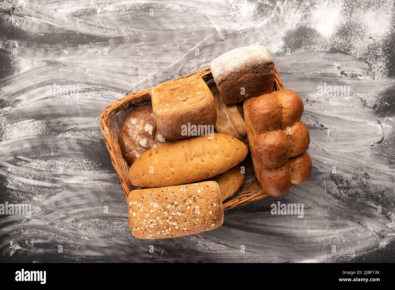 Basket with fresh bread on table against black background. Bakery products in straw basket