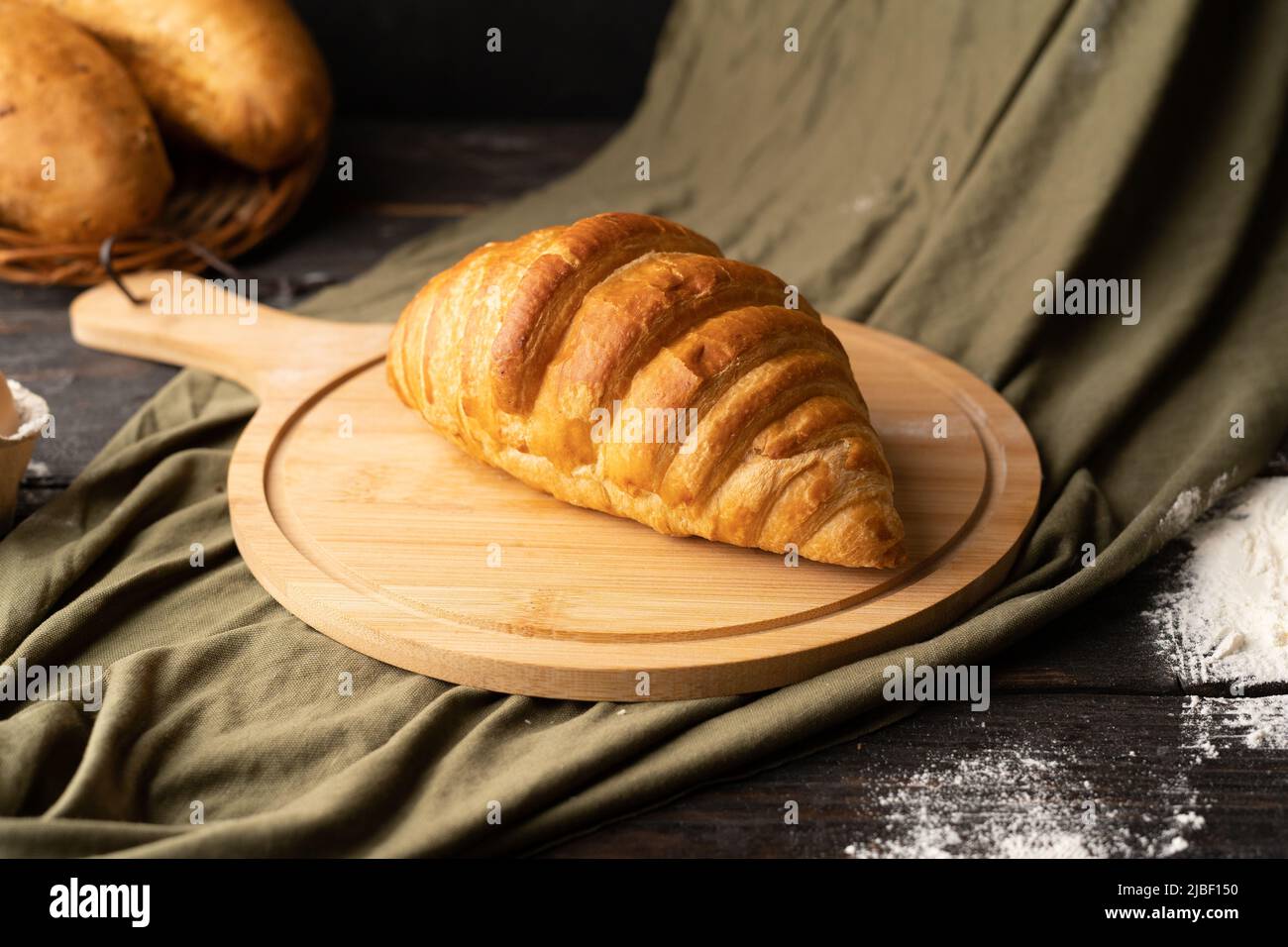 fresh croissant on wooden board, green fabric background, homemade baking Stock Photo