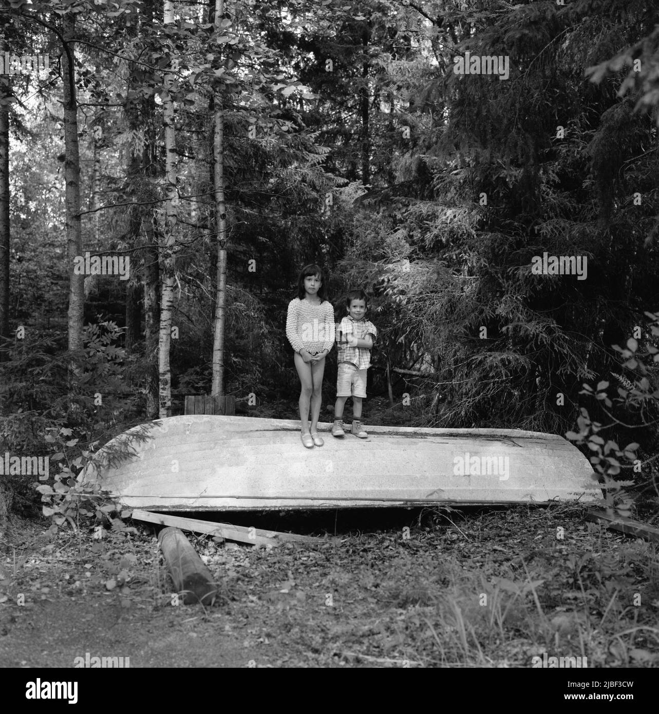 Children standing on overturned boat in forest Stock Photo