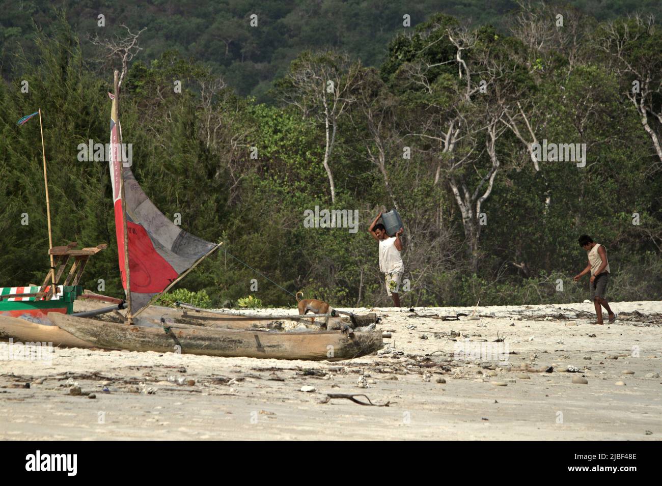 A fisherman carrying a jerry can as he is walking toward wooden canoes on Tarimbang beach in Tabundung, East Sumba, East Nusa Tenggara, Indonesia. Stock Photo