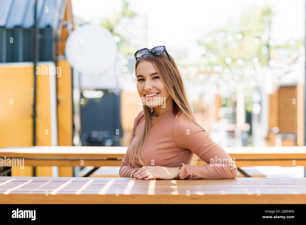 A young smiling woman sits on the terrace of a street cafe in summer ...