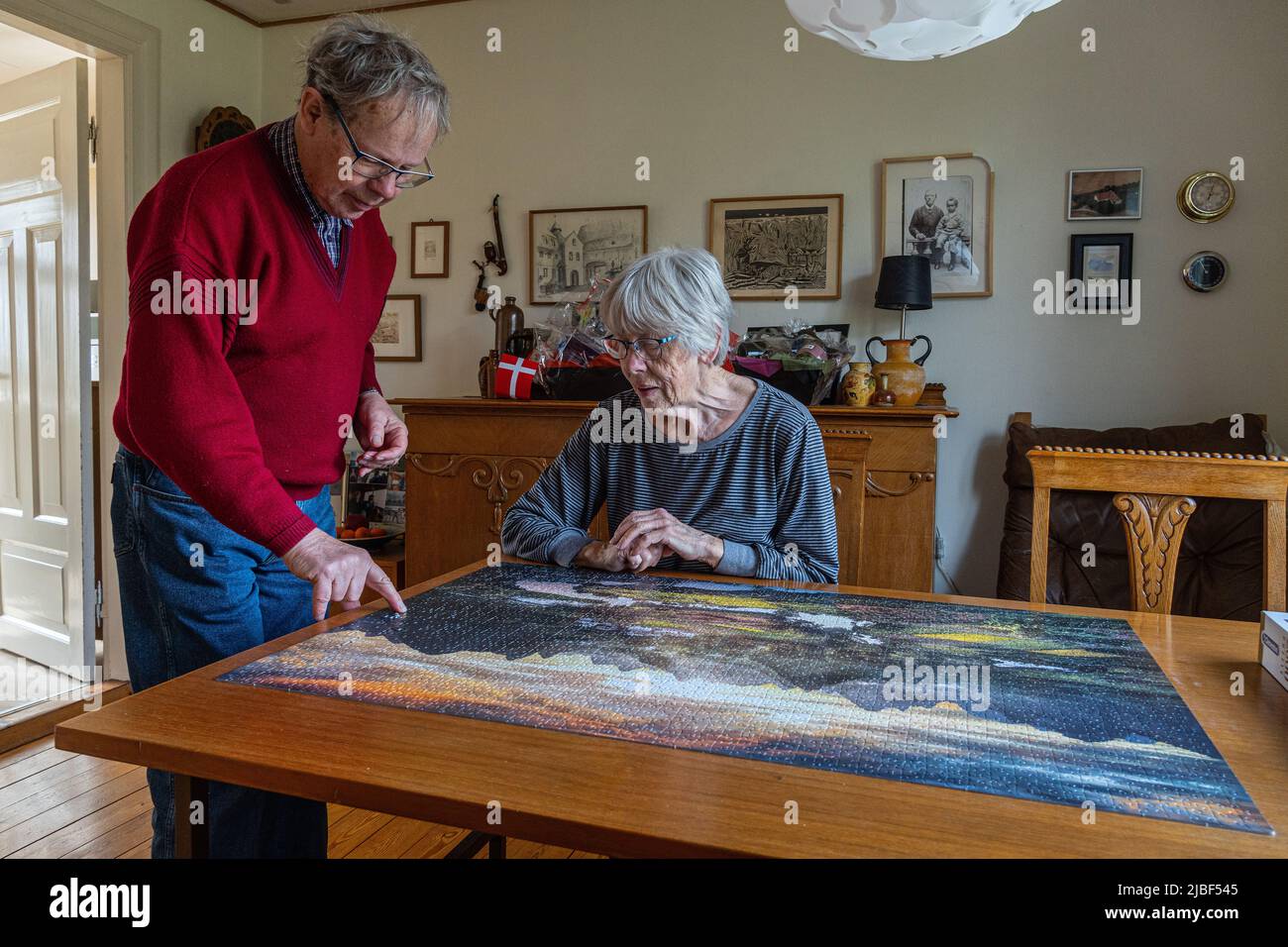 An elderly Danish couple completes a large puzzle at home on the wooden table. Assens, Fynn, Denmark, Europe Stock Photo