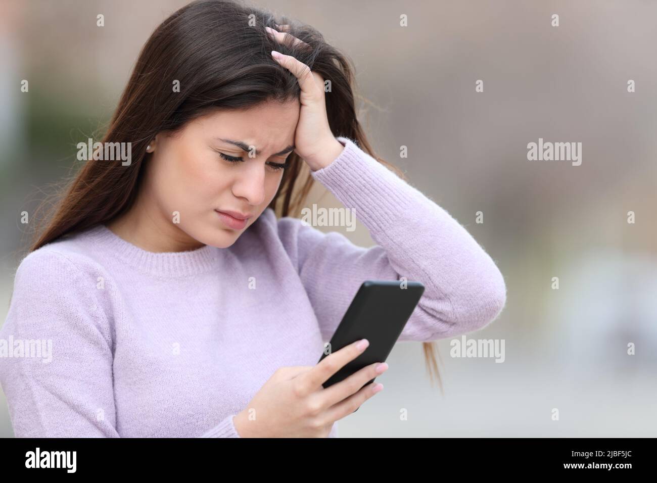 Worried teen checking bad news on smart phone in the street Stock Photo
