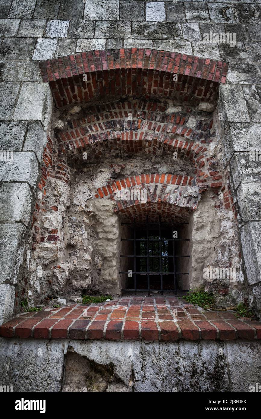 Barred recessed window in medieval castle, old stone structure with brick elements in arches and windowsill. Stock Photo