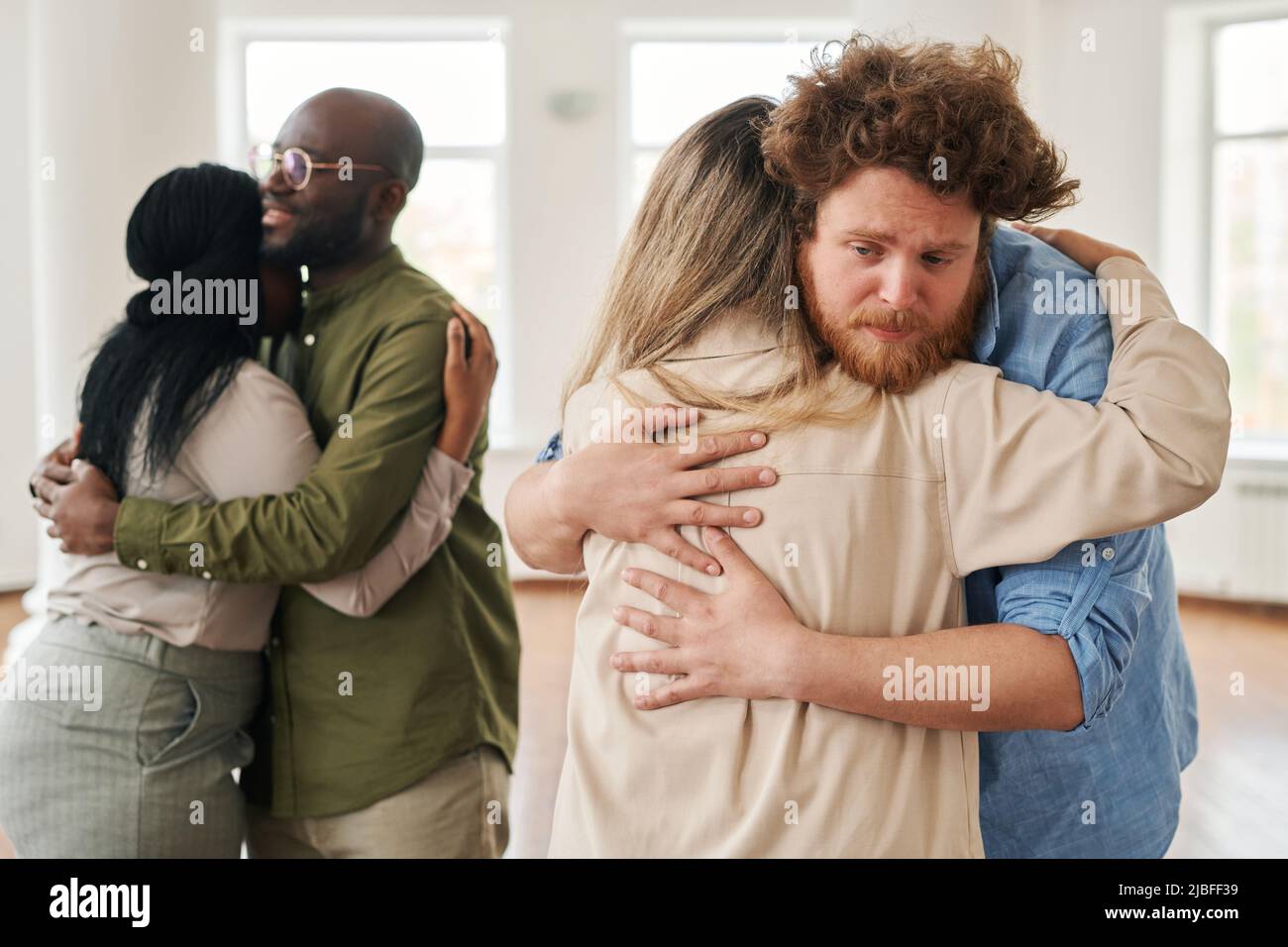 Young man giving hug to female against African American patients standing in embrace while attending course of psychological help Stock Photo