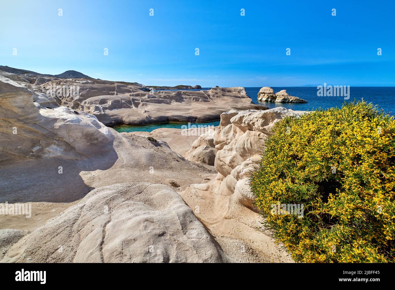 Beautiful white rocks of Sarakiniko beach, Aegean sea, Milos island, Greece. No people, empty cliffs, summer sunshine, clear sea waters, bush, flowers Stock Photo