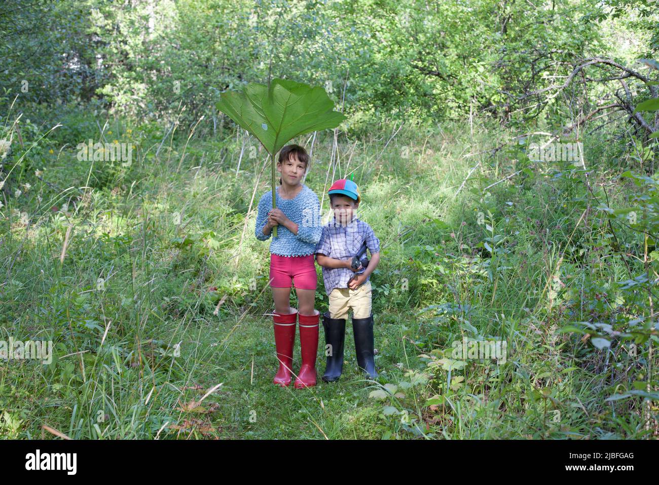 Boy and girl with large leaf in forest Stock Photo