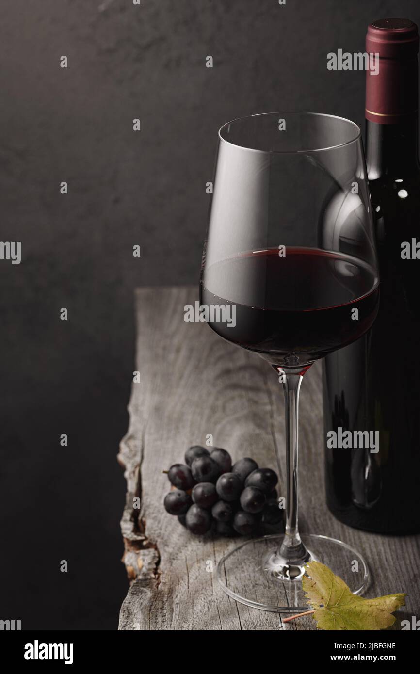 A glass of red wine, grapes and a bottle on an old wooden table. Dark ...