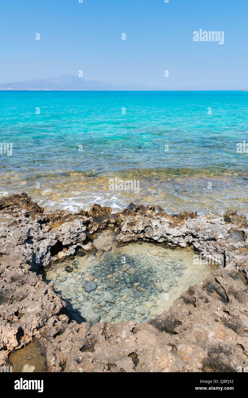 Natural water puddle on the rocky beach of Chrissi island. Beautiful turquoise Mediterranean sea in the background. Crete, Greece. Stock Photo