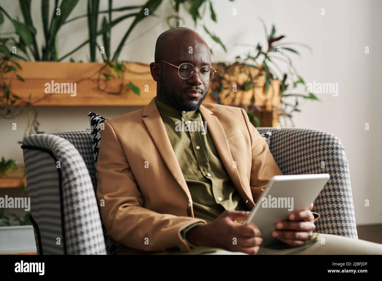 Young confident professional psychologist in formalwear having online session with patient while sitting in armchair in his office Stock Photo