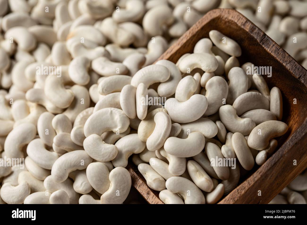 Top view of wooden cup full of healthy dried uncooked white bean seeds stacked together Stock Photo