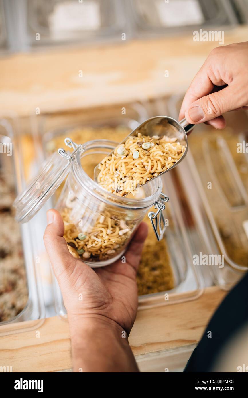 Back view of anonymous female pouring dry pasta inside glass jar in local store Stock Photo