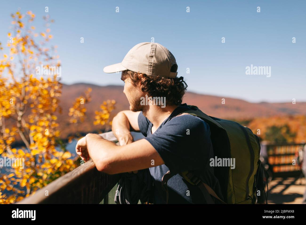 Side view of dreamy male tourist standing on wooden footbridge over lake while admiring natural landscape in Canada Stock Photo