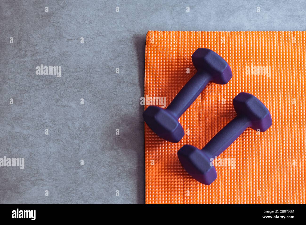 Top view of violet dumbbells and orange mat placed on gray floor during fitness workout Stock Photo