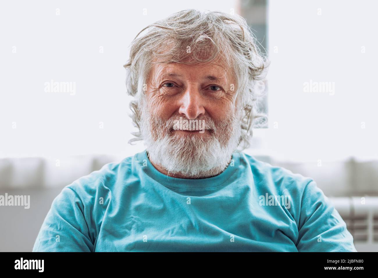Elderly male with gray beard against blurred background looking at camera at home Stock Photo