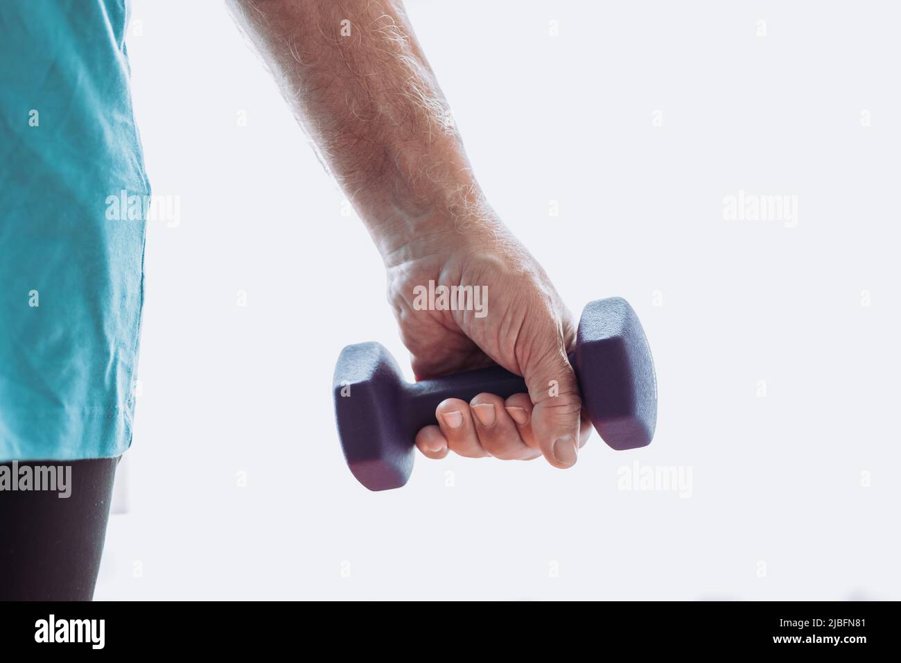 Cropped unrecognizable senior male arm in sportswear doing exercise with dumbbells during fitness workout in morning at home Stock Photo