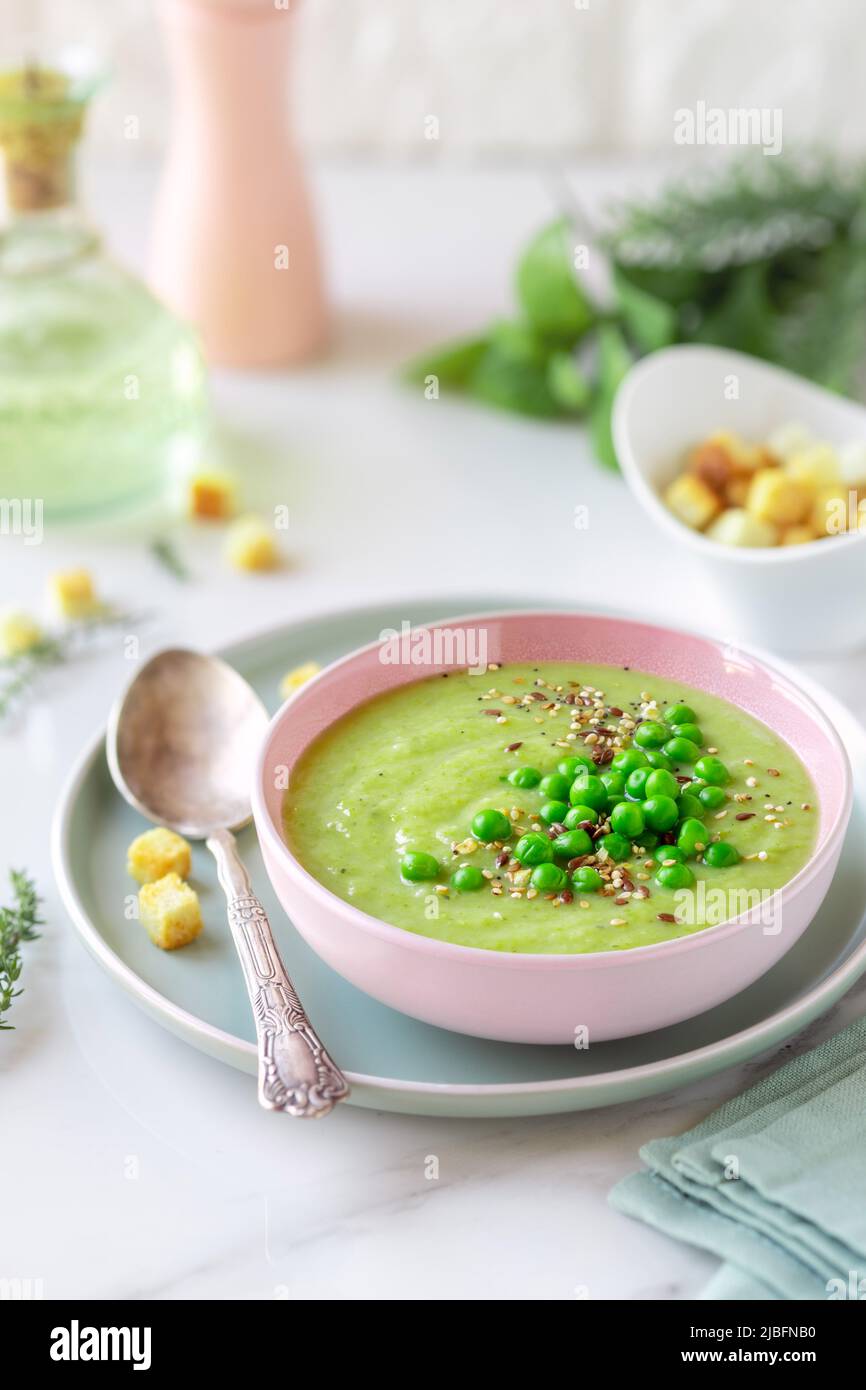 Delicious healthy cream pea soup in a bowl garnished with green peas and croutons on table Stock Photo