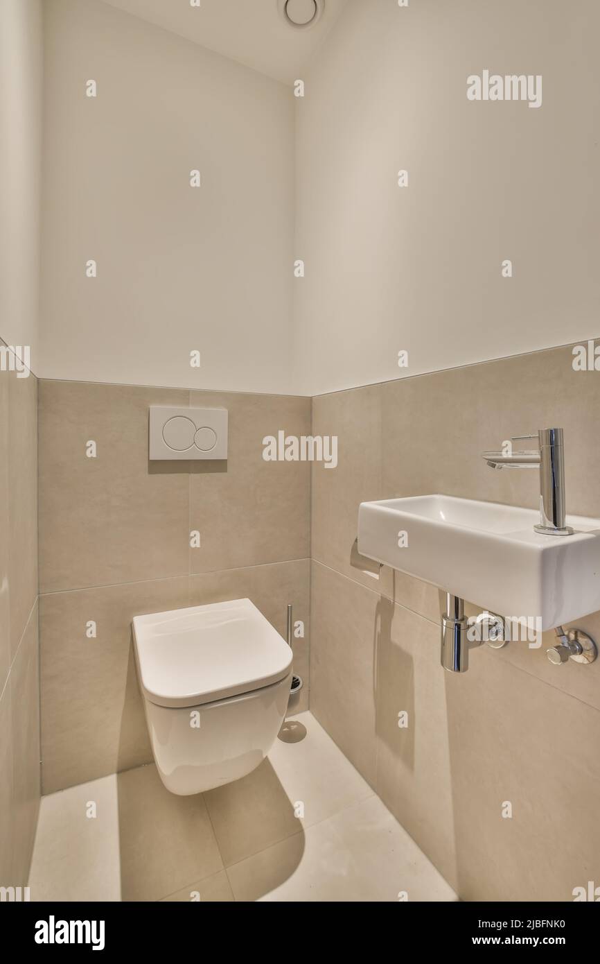 White ceramic sink placed at tiled wall in light stylish bathroom with toilet at home Stock Photo