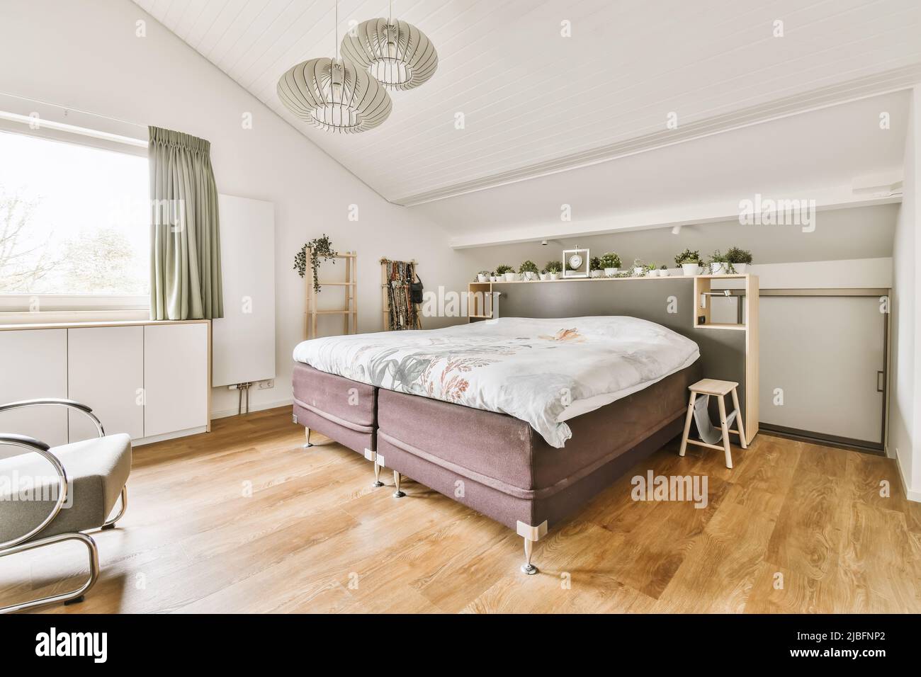 Comfortable bed located in sunlit modern bedroom with furniture and