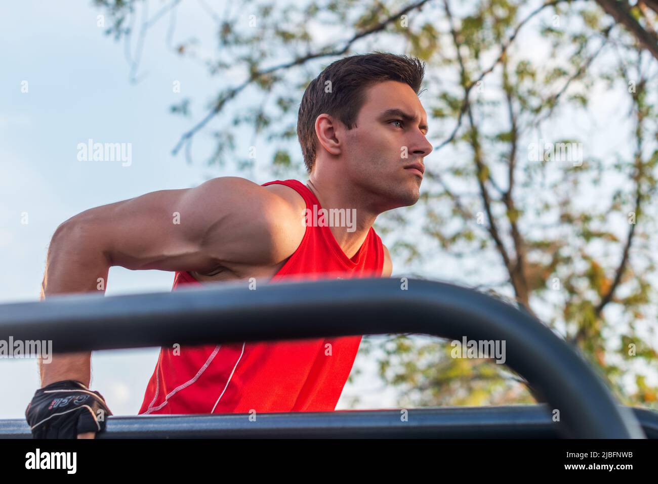 Fit man doing triceps dips on parallel bars at park exercising outdoors. Stock Photo